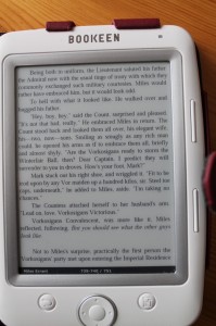 Kirjaa lukemassa. Sivua käännetään oikeassa laidassa olevilla napeilla, ja alalaidan napeista pääsee selaamaan kirjastoa ja säätämään laitteen asetuksia.