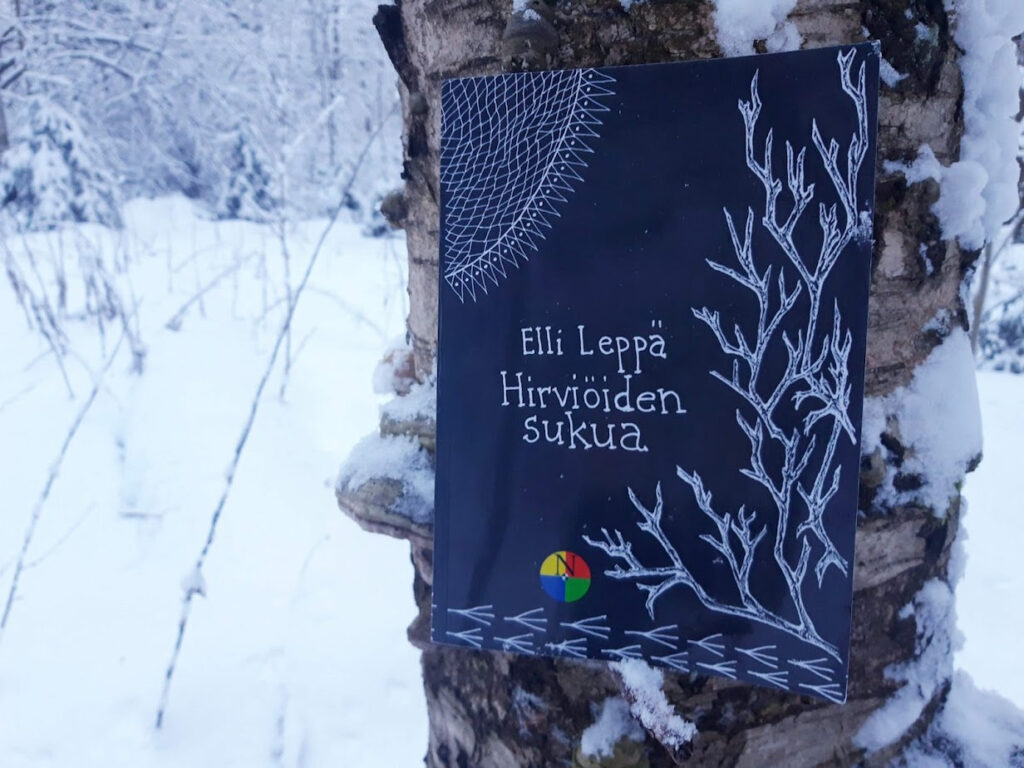 Kirja nojaa koivua vasten lumisessa metsässä.